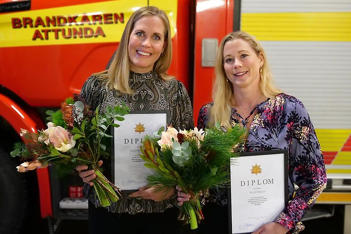 Två tjejer som är mottagare av priset framför en brandbil från Attunda brandkår