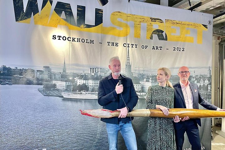 Bild på Fredrik Kjos och två personer till framför bild över Stockholms innerstad med wallstreets logga på